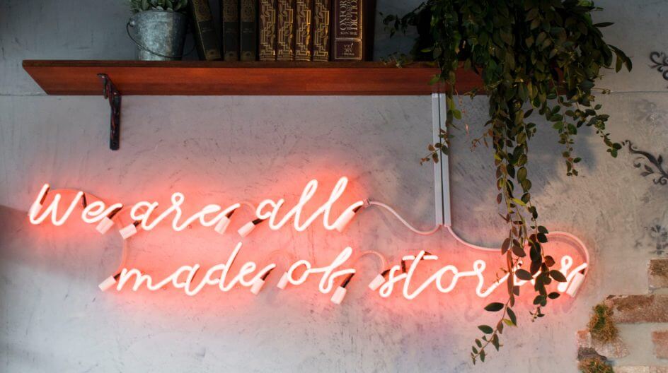 Wall with neon sign that says "We are all made of stories"