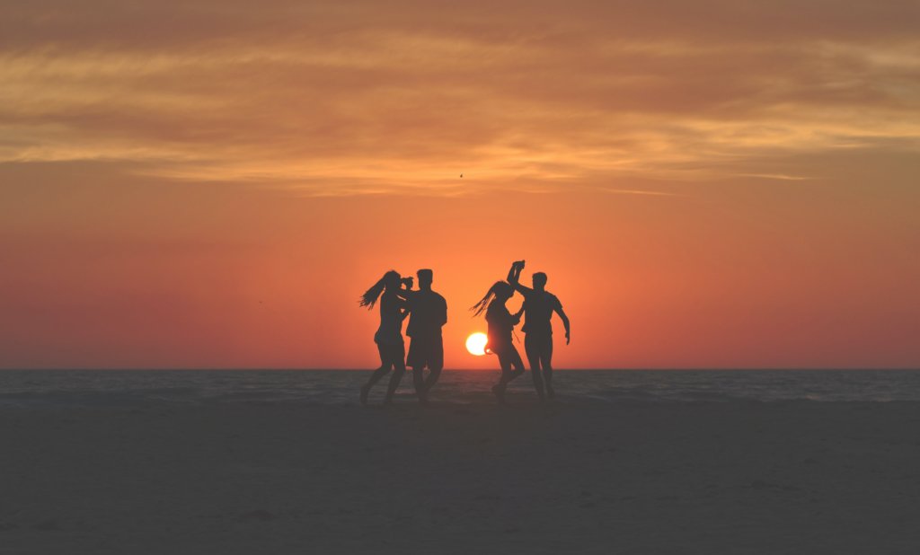 Two couple dancing on the beach with the sun setting in the backgound