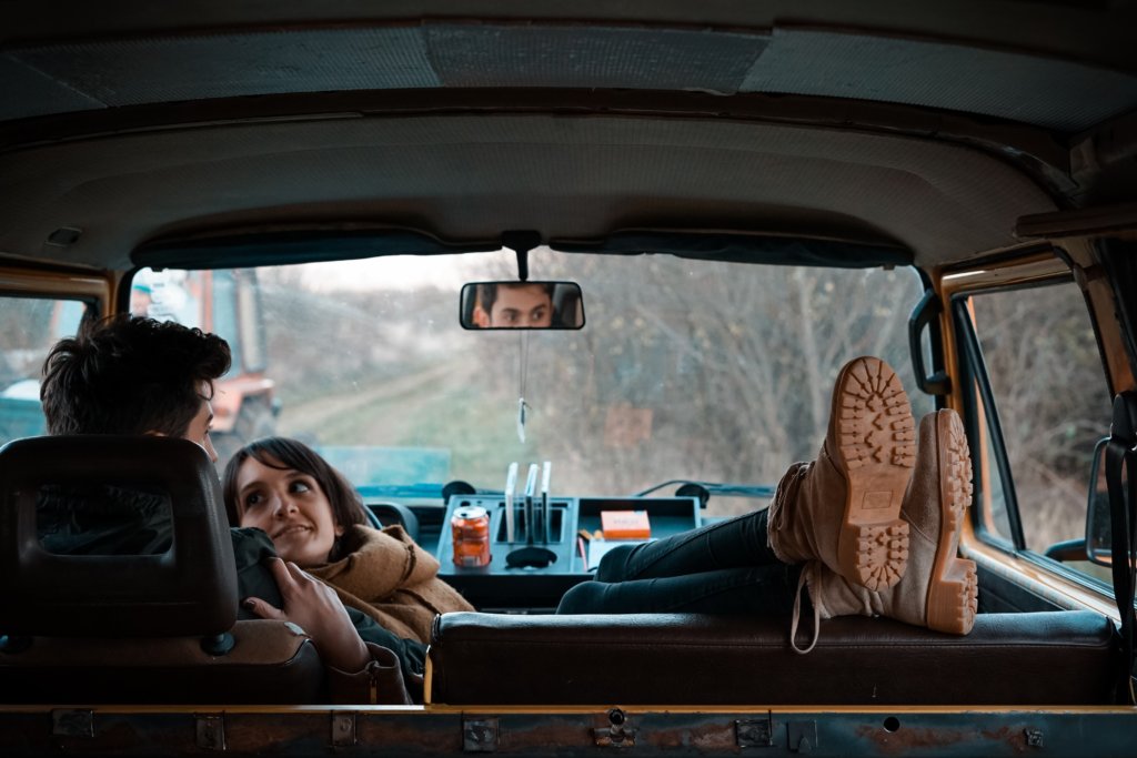 A couple sitting in a van on the side of the road while the woman looks longingly at the man's face