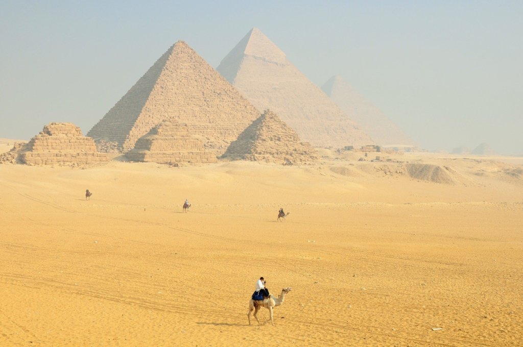 A view of the pyramids of Giza with a few people riding camels in the foreground