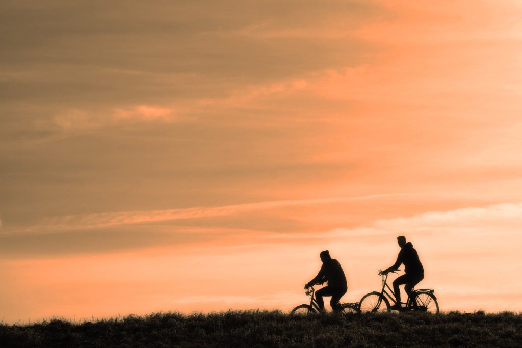 Two people riding bicycles with an orange sky in the background