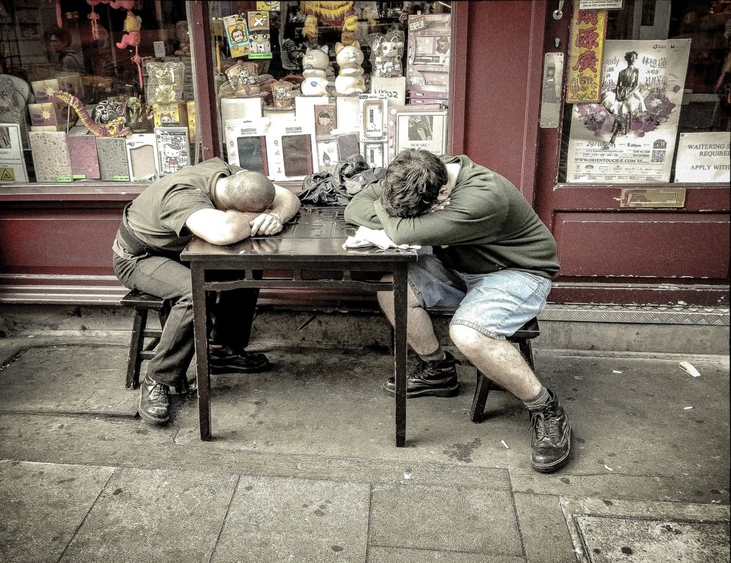 Two men asleep at a table on a sidewalk outside a store