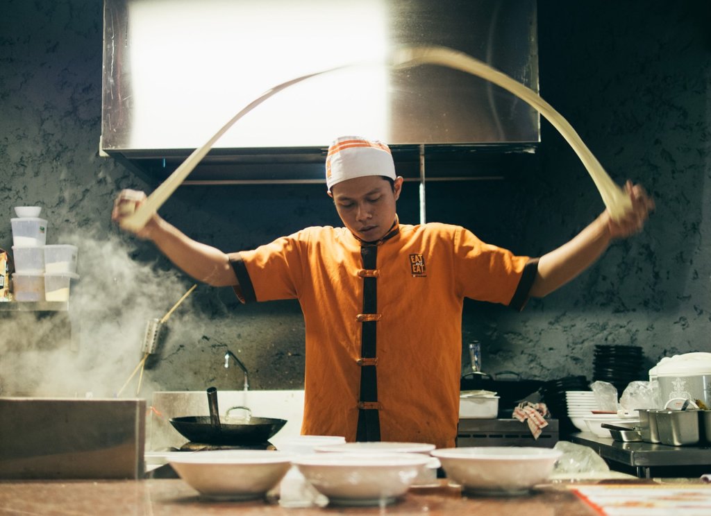 A chef tossing noodle dough into the air