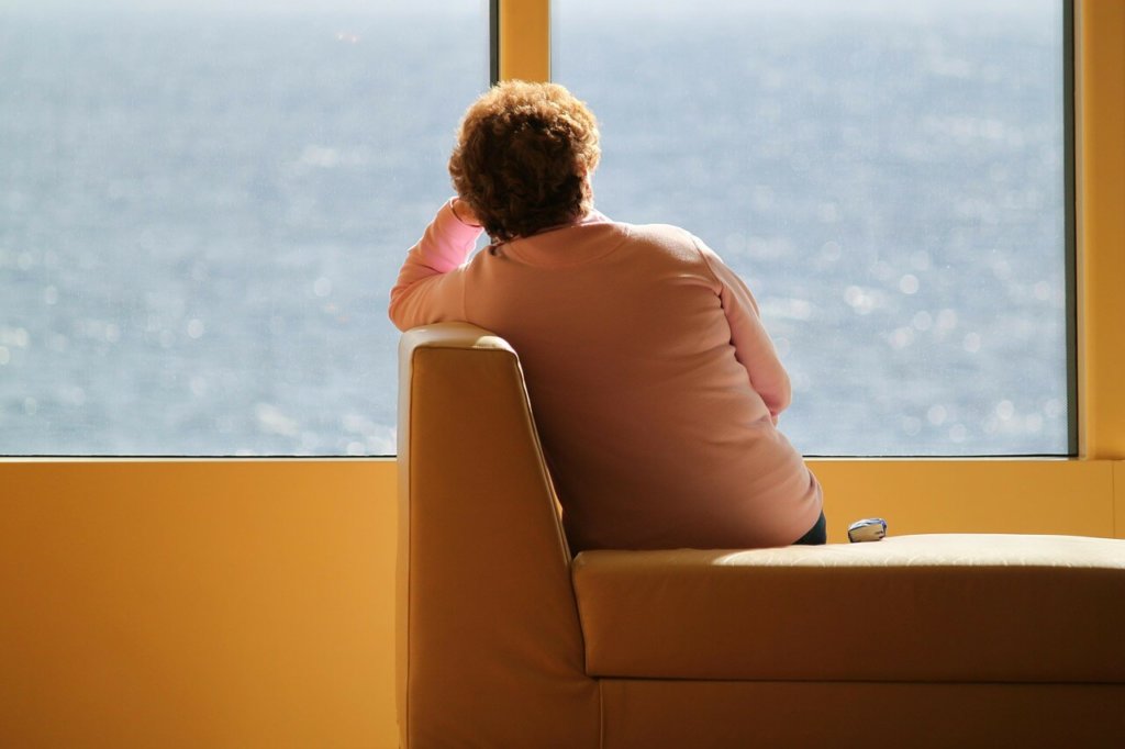 A woman sitting alone with her back facing the camera, head propped up by her arm, and staring out a window 